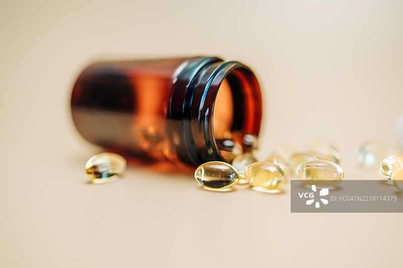 鱼油、维生素D、Omega-3胶囊从棕色塑料瓶中洒落在米色背景上图片素材