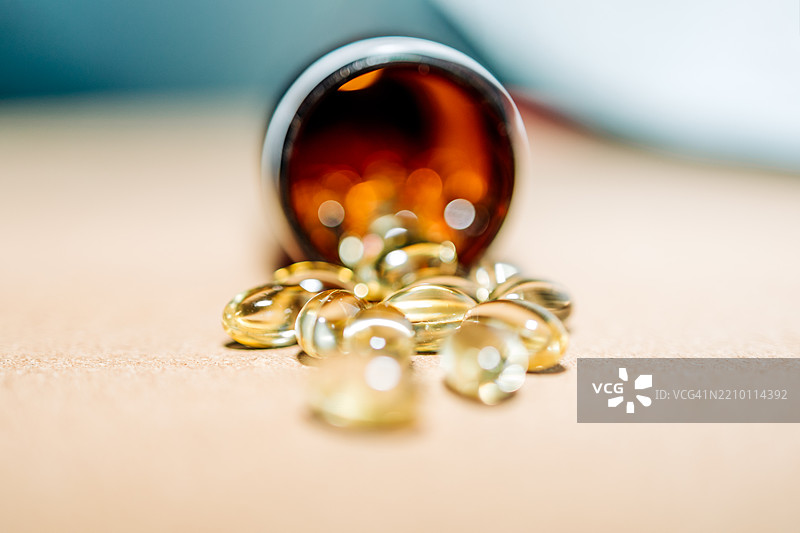 鱼油、维生素D、Omega-3胶囊从棕色塑料瓶中洒落在米色背景上图片素材