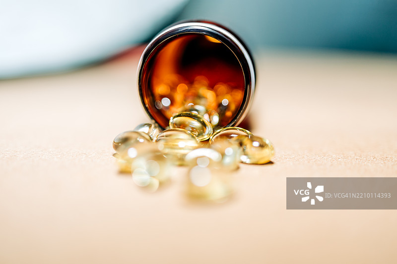 鱼油、维生素D、Omega-3胶囊从棕色塑料瓶中洒落在米色背景上图片素材