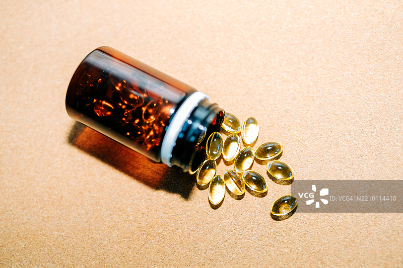 鱼油、维生素D、Omega-3胶囊从棕色塑料瓶中洒落在米色背景上图片素材