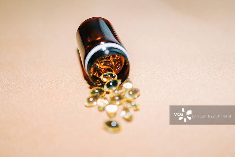 鱼油、维生素D、Omega-3胶囊从棕色塑料瓶中洒落在米色背景上图片素材