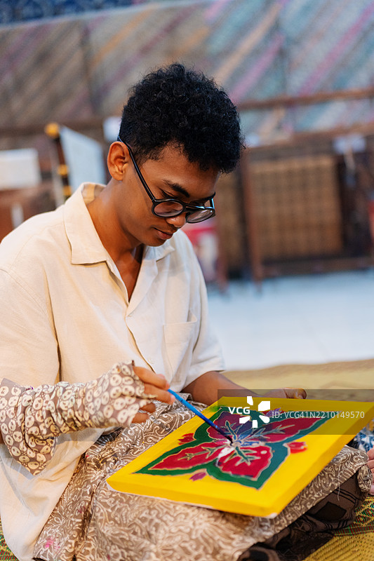 东南亚男子穿着保护性巴蒂克袖子，正在用大胆的天然染料为画布上色图片素材