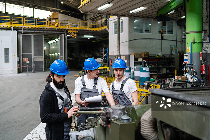 穿着防护装备的机械师们在车间内协作，认真专注地检查工业设备。图片素材