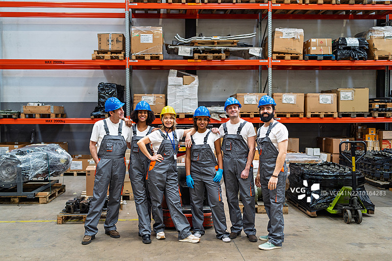 穿着防护装备的仓库团队自信地摆姿势，微笑着进行工作场所安全时刻。图片素材