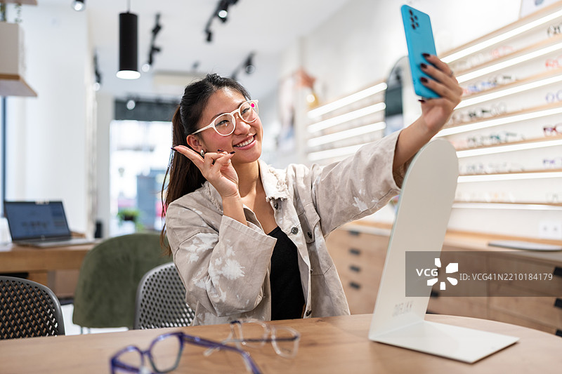 年轻女性在眼镜店里戴着新眼镜自拍图片素材