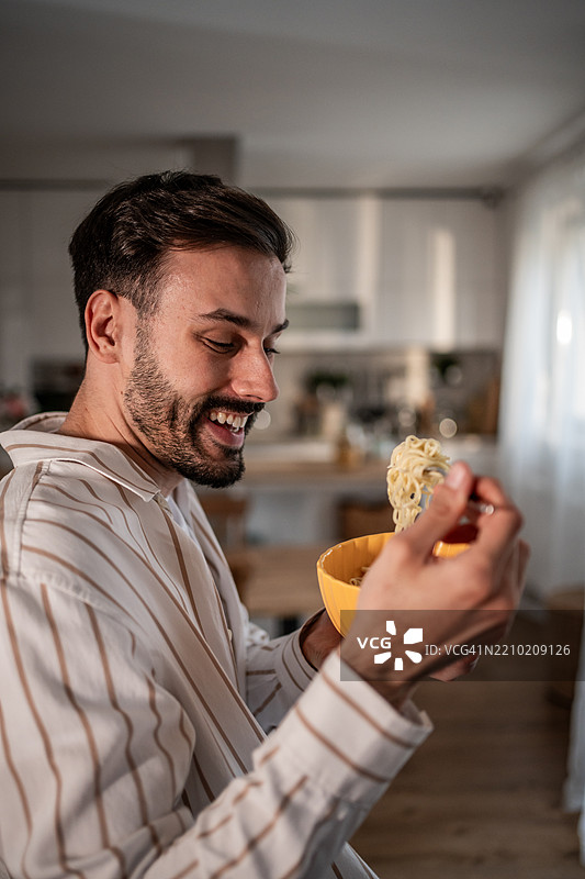 快乐的年轻人在厨房里享受一碗面条图片素材