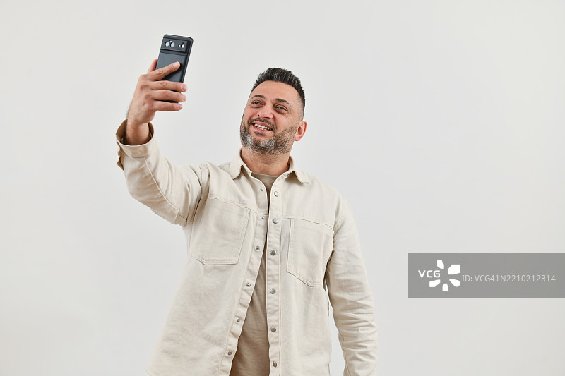 帅气的男性在白色摄影棚背景下用智能手机拍自拍图片素材