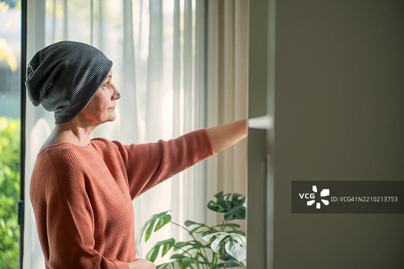 老年癌症患者站在窗边感受希望。图片素材