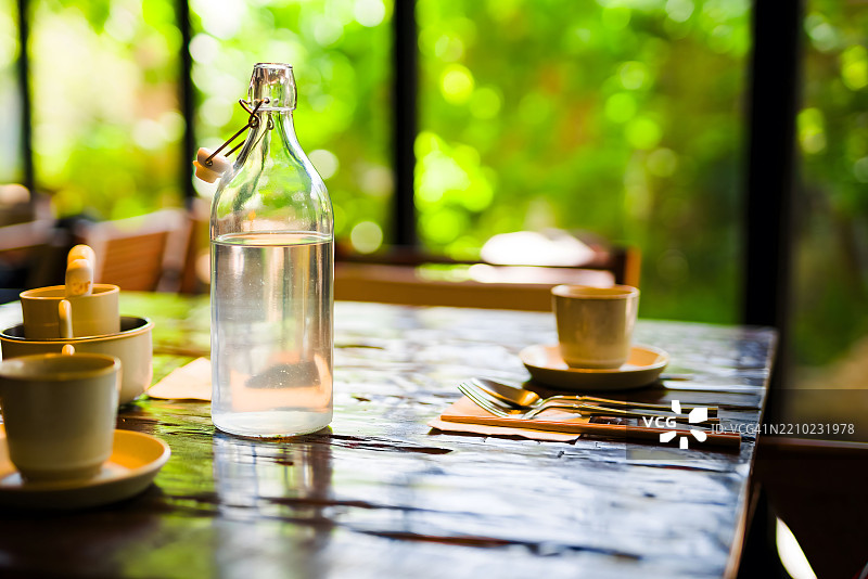 餐厅餐桌上的玻璃瓶和餐具，背景是模糊的绿色植物图片素材