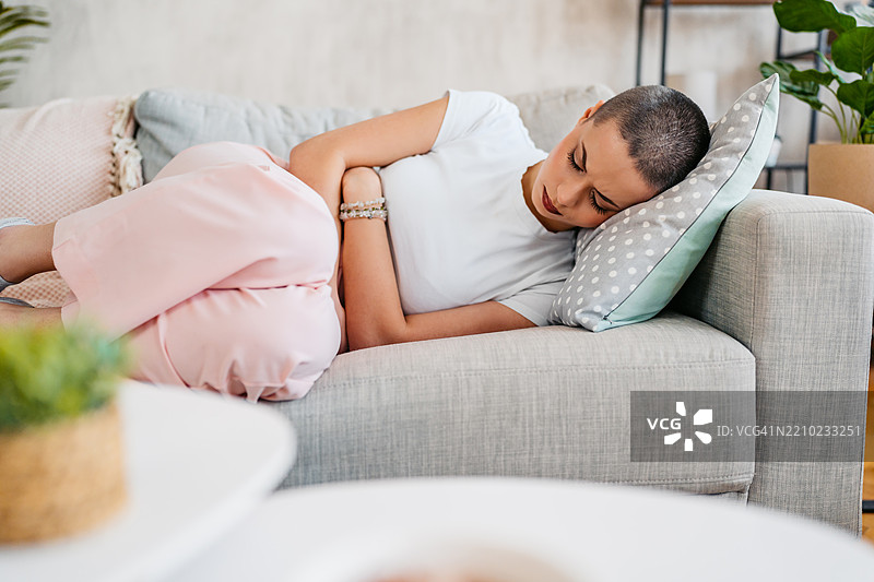 年轻女性在家中因月经疼痛而感到不适，剃短发。图片素材