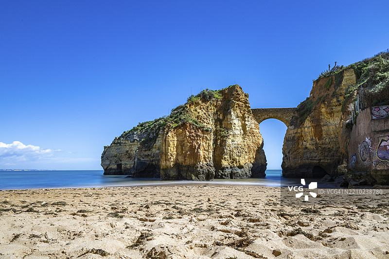 沙滩上的黄色岩石和悬崖。一个海湾，古老的皮尼昂堡石桥连接着两座悬崖。卡尔德拉海滩，拉各斯。阿尔加维，葡萄牙，欧洲图片素材