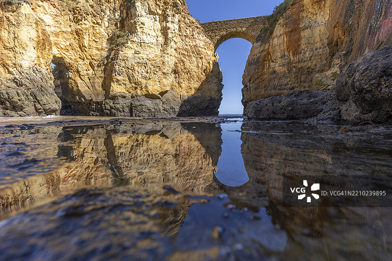 沙滩上的黄色岩石和悬崖。海边的一个海湾,古老的皮尼昂堡石桥连接着两座悬崖。卡尔德拉海滩,拉各斯。阿尔加维,葡萄牙,欧洲图片素材