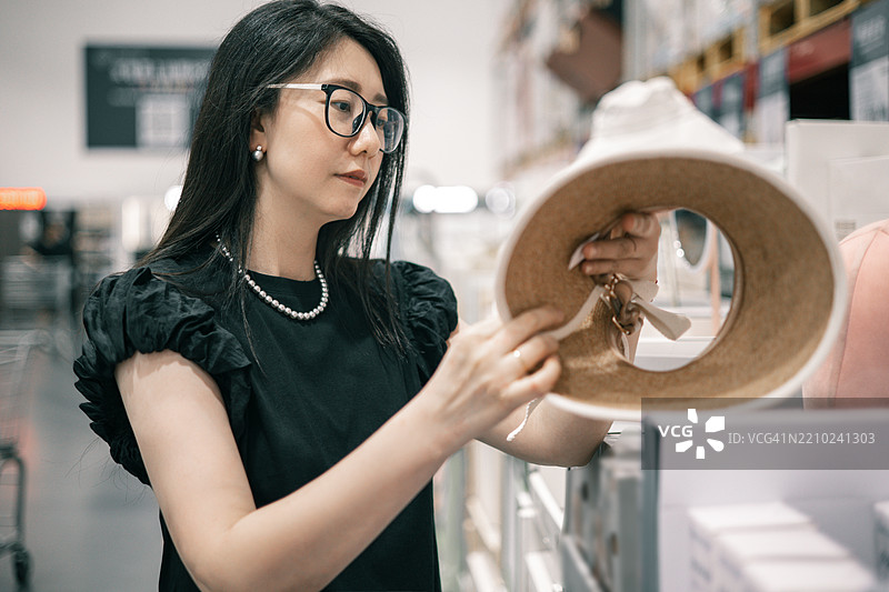 一位亚洲女性在超市挑选太阳帽图片素材