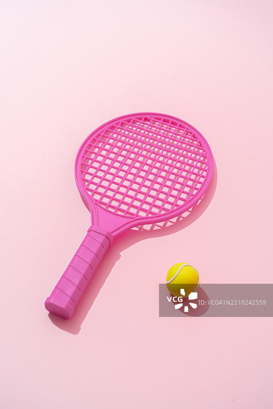 粉色网球拍和黄色网球躺在粉色背景上图片素材
