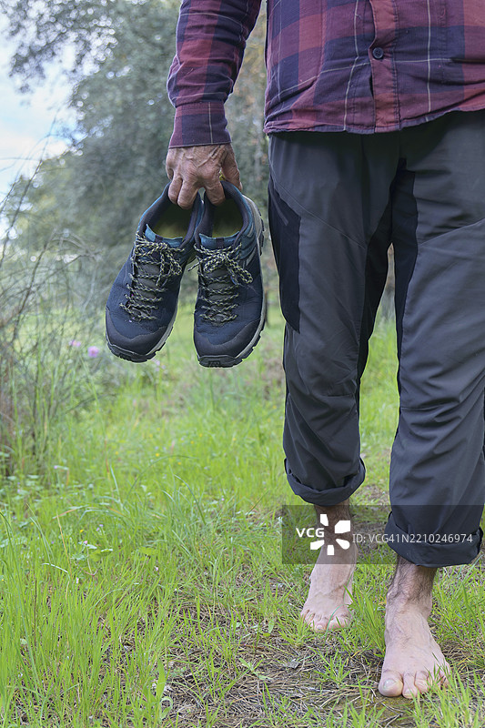 徒步旅行者赤脚在草地上漫步，手里拿着他的登山鞋图片素材