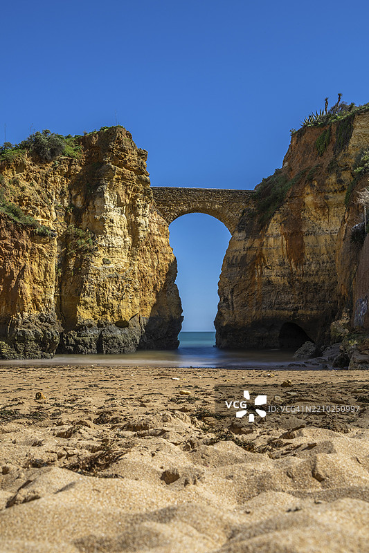 沙滩上的黄色岩石和悬崖。海边的一个海湾,古老的皮尼昂堡石桥连接着两座悬崖。卡尔德拉海滩,拉各斯。阿尔加维,葡萄牙,欧洲图片素材