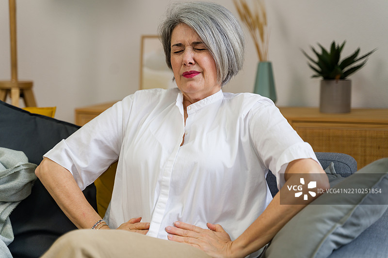 坐在家中沙发上的老年女性因腹痛而感到不适图片素材