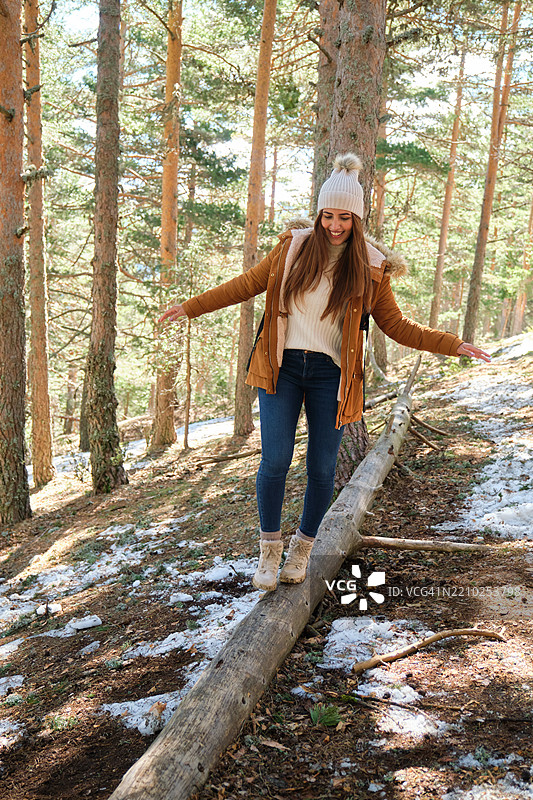 年轻女性在冬季雪林中平衡在一根木头上图片素材