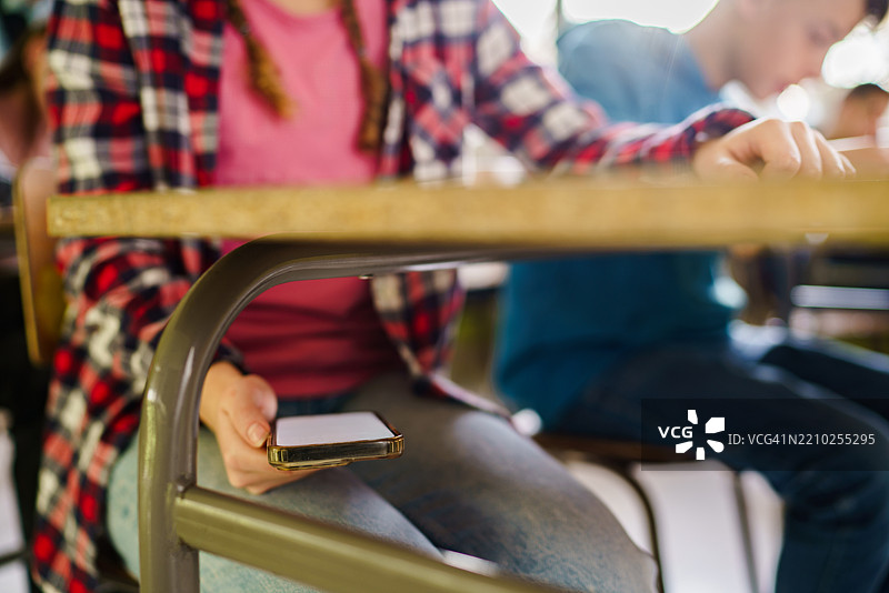 女孩在课堂上桌子下使用手机图片素材