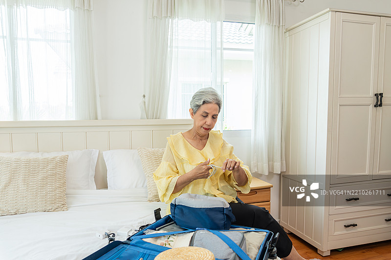 年长的亚洲女性正在为即将到来的独自旅行打包配件和必需品图片素材