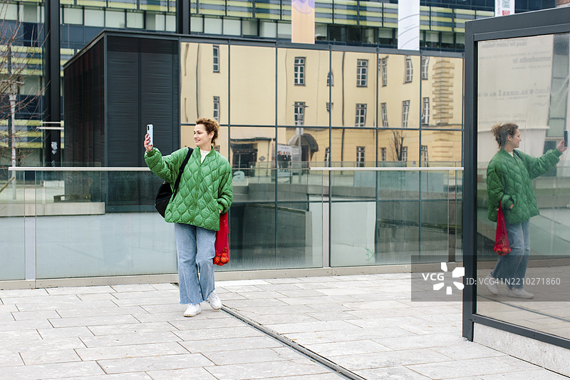 身穿绿色夹克的千禧女性在城市中漫步图片素材