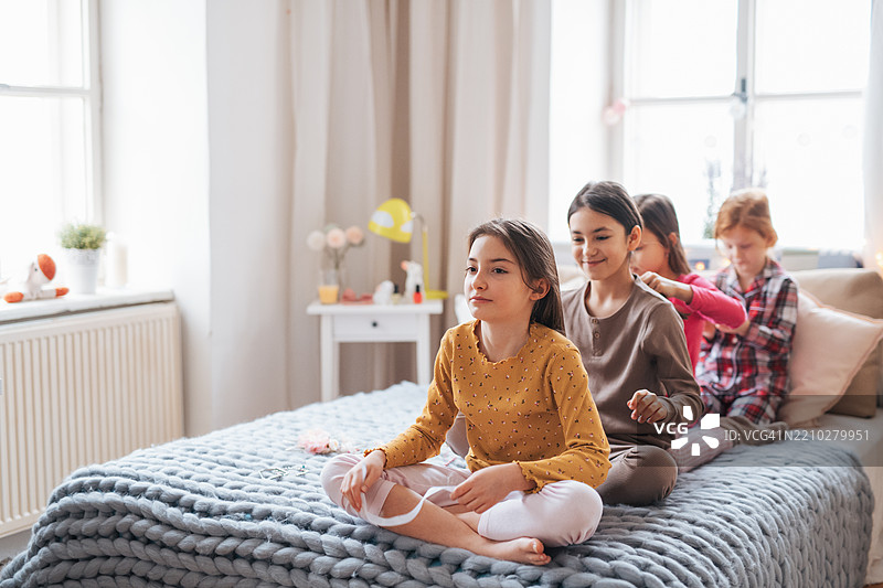 Four friends braiding each other’s hair while sitting on the bed.图片素材