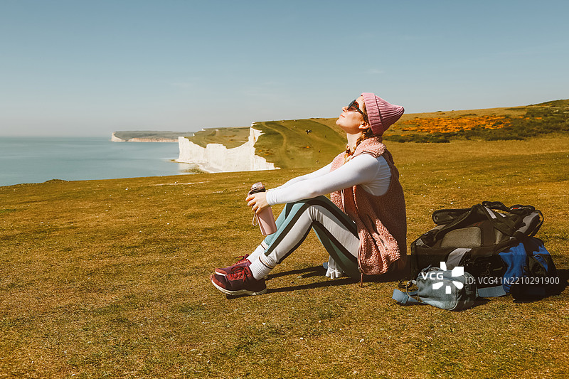 女人在海岸悬崖顶上放松，阳光洒在她的脸上图片素材