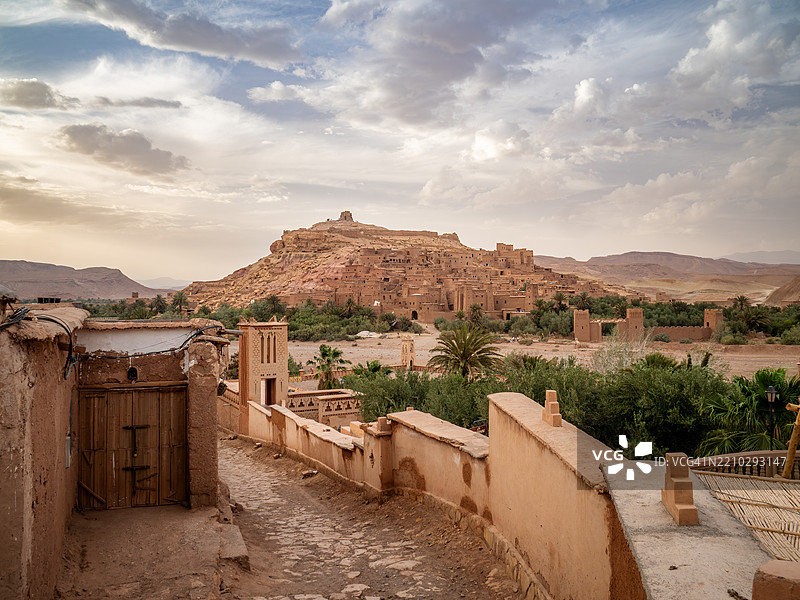 日落时分,俯瞰阿伊特·本哈杜镇的鹅卵石街道,两旁是传统建筑,背景是古老的柏柏尔人防御村落和卡斯巴(阿伊特·本哈杜卡斯巴),联合国教科文组织世界遗产 - 瓦尔扎扎特 - 摩洛哥。图片素材