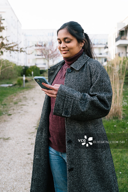 年轻女性穿着休闲外套，低头看着她的智能手机。图片素材