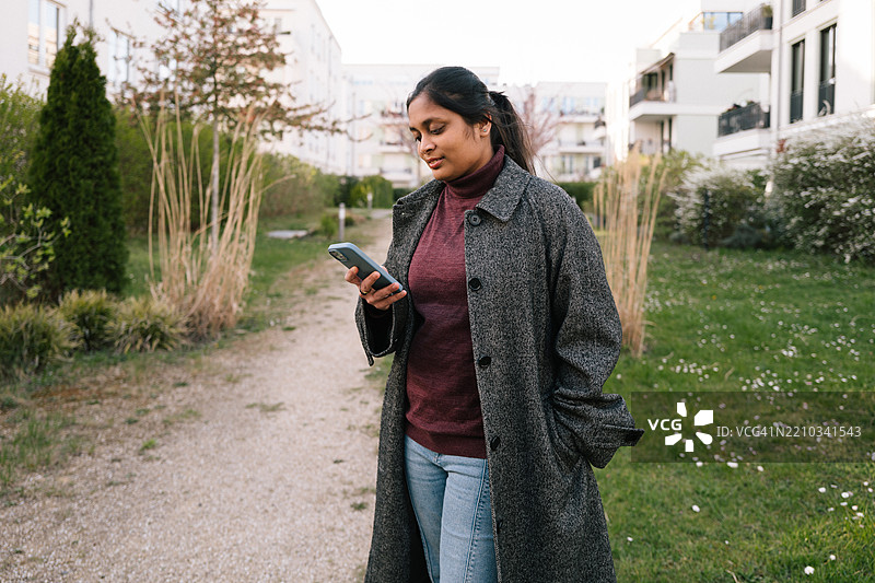 年轻女性穿着休闲外套，低头看着智能手机。图片素材