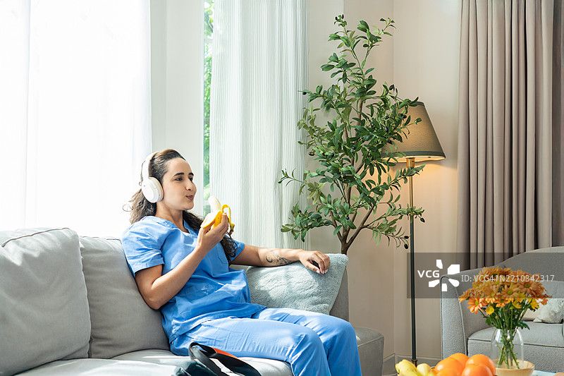 放松的护士在家享受健康的小吃/香蕉并听音乐图片素材