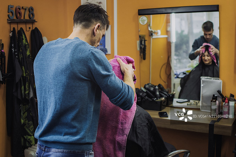 男发型师在美容院为女性顾客吹干头发。小型美发沙龙。图片素材