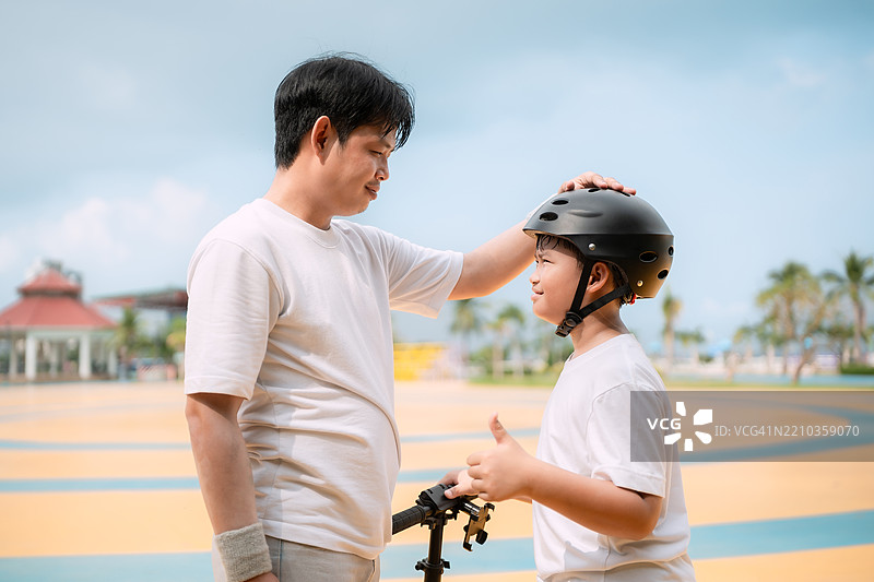 父亲在滑板公园帮助儿子戴上头盔图片素材