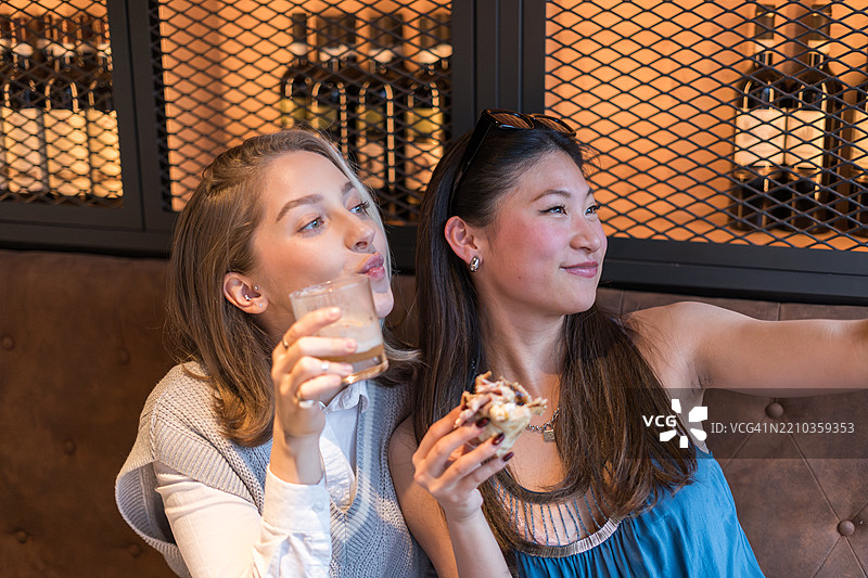 两位年轻女性在酒吧里喝酒吃东西时自拍图片素材