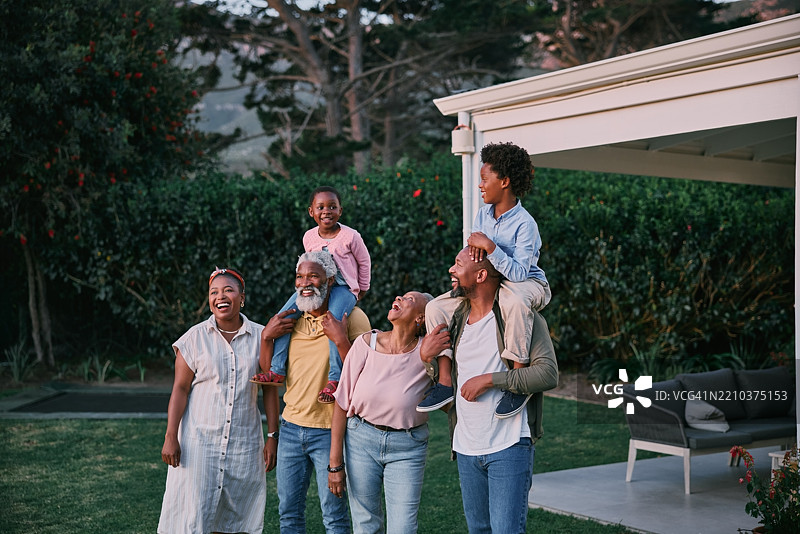 黑色家庭，肩上扛着孩子们，在后院享受自然风光，快乐或亲密。孩子、父母和祖父母在户外花园中一起分享幸福、关爱或欢笑。图片素材