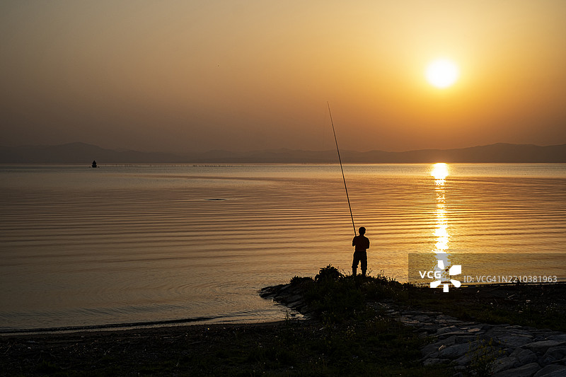 日落时分，渔夫在海滩上投掷钓竿的剪影图片素材