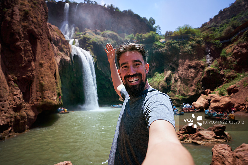 在摩洛哥的乌祖德瀑布前，一名游客开心地对着相机自拍。图片素材