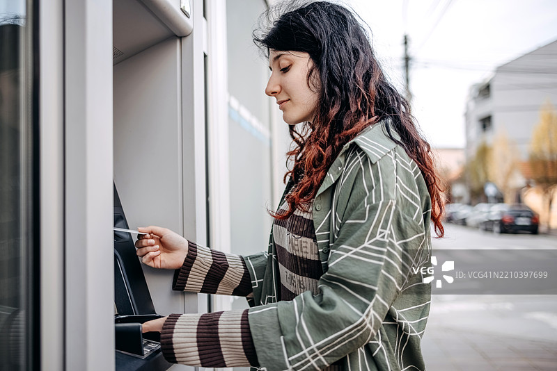 少女在户外的ATM机前取钱。图片素材