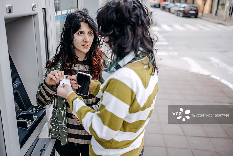 少女在户外的ATM机前取款，正在使用信用卡。图片素材