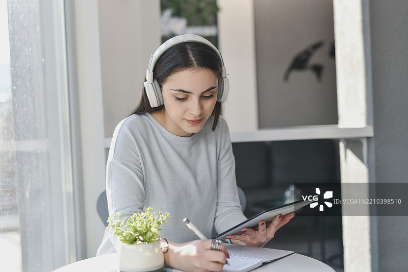 专注的女学生正在用平板电脑写笔记，同时戴着耳机听音乐图片素材