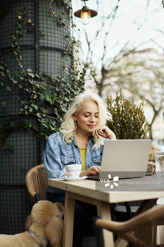 一位五十多岁的美丽女性坐在咖啡馆的花园里，正在使用笔记本电脑工作。图片素材