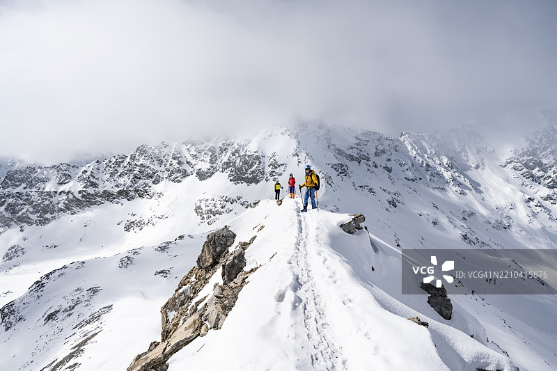 三名登山者攀登皮兹·拉维纳尔的狭窄山脊，冬季山景的全景，格劳宾登高路线，阿尔布拉阿尔卑斯山，瑞士拉赫丁阿尔卑斯山，格劳宾登，瑞士东部，欧洲图片素材