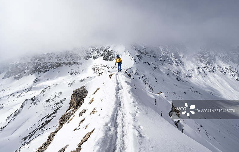 登山者攀登皮兹·拉维纳尔的狭窄山脊,冬季山景一览无余,格劳宾登高路线,阿尔布拉阿尔卑斯山,瑞士莱蒂安阿尔卑斯山,格劳宾登,瑞士东部,欧洲图片素材