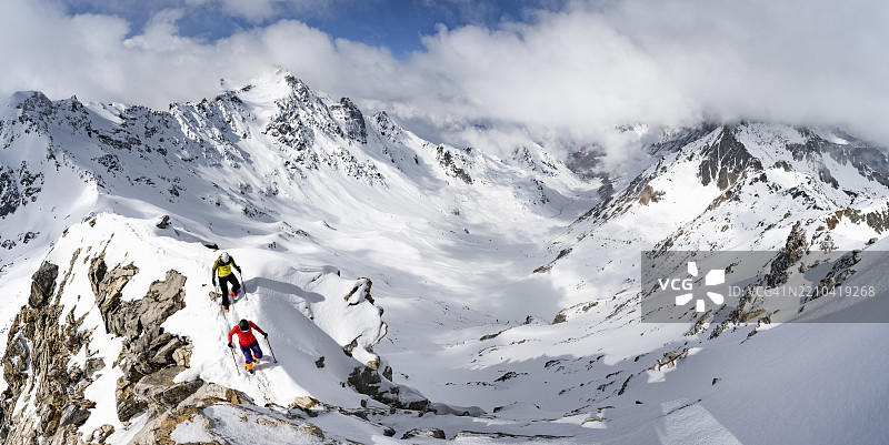 两名登山者攀登皮茨·拉维纳尔的狭窄山脊,冬季山地风景中的山脉全景,格劳宾登高路线,阿尔布拉阿尔卑斯山,瑞士莱蒂安阿尔卑斯山,格劳宾登,瑞士东部,欧洲图片素材