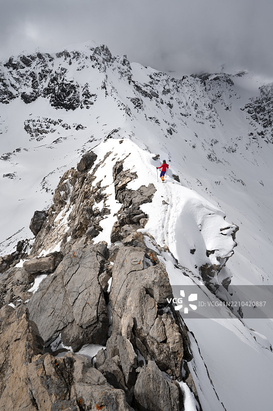 登山者在皮茨·拉维纳尔的狭窄山脊上下降,冬季山景中壮丽的山脉全景,格劳宾登高路线,阿尔布拉阿尔卑斯山,瑞士莱蒂安阿尔卑斯山,格劳宾登,瑞士东部,欧洲图片素材