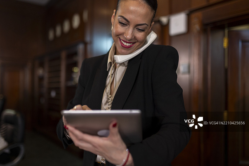 微笑的女接待员一边打电话一边在系统中记录预订信息图片素材
