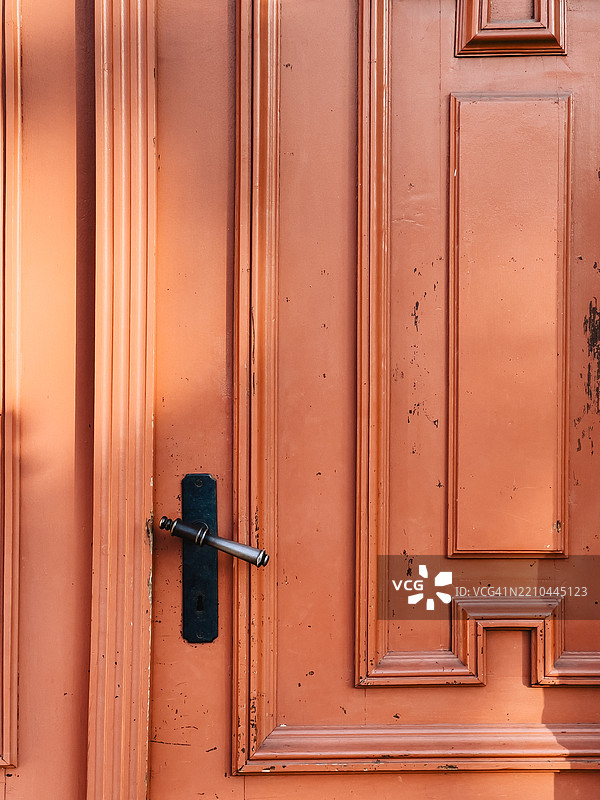 阳光照耀着一扇古老、风化的橙色木门，门上有经典的金属把手和钥匙孔。图片素材