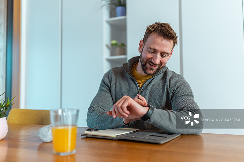 中年白人男性在家餐桌上使用智能手表，面带轻松表情图片素材