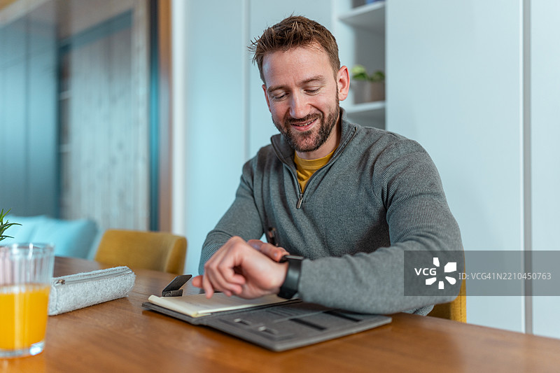 微笑的中年男子在自然光照射下的舒适餐厅中使用智能手表图片素材