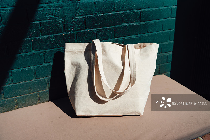 一只可重复使用的购物袋放在绿色砖墙旁的长椅上图片素材